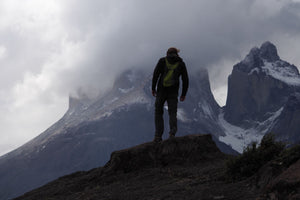 Man with backpack standing high up in the cloudy mountains looking out 