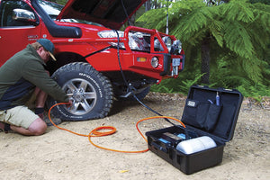 Red overland vehicle with guy inflating his tire with portable ARB compressor