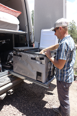 Back doors of a Sprinter van open with a guy digging in his Snomaster fridge pulled out on a slider.